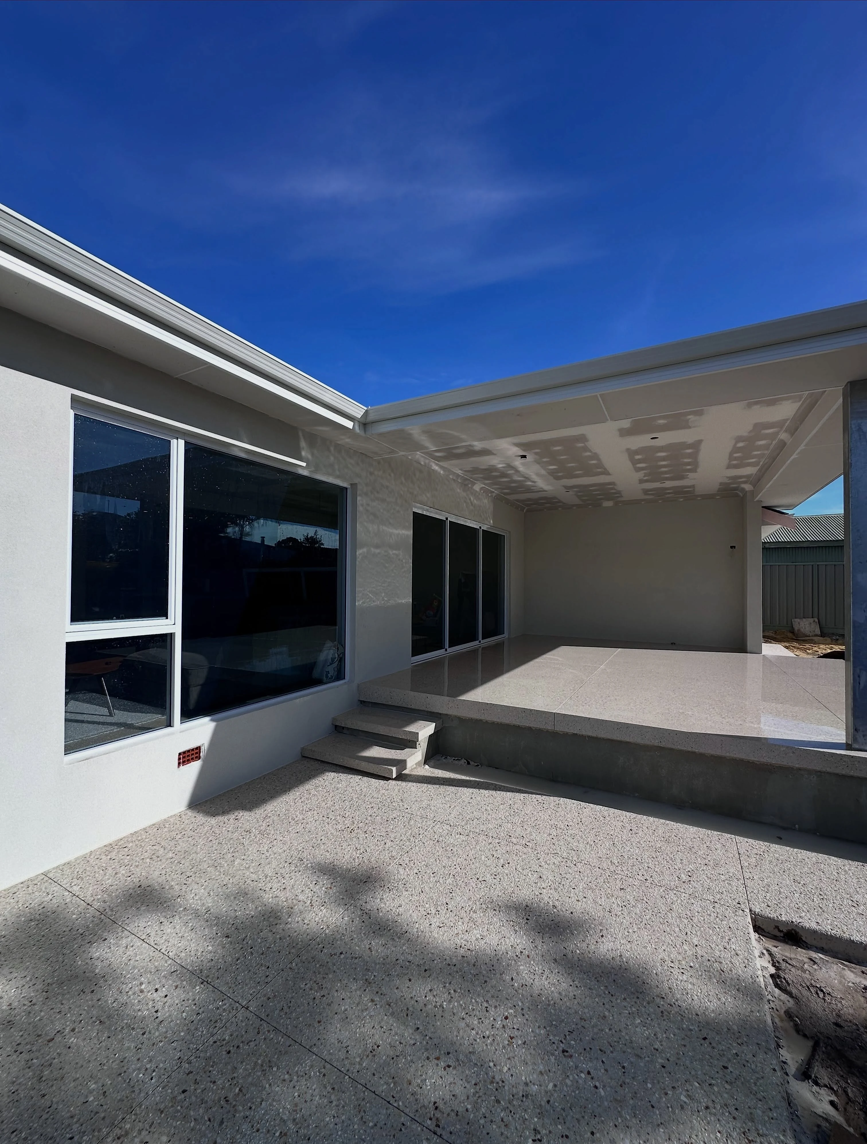Honed alfresco and driveway in Limecrete Coral White, replacing the original surface across the whole rear ent