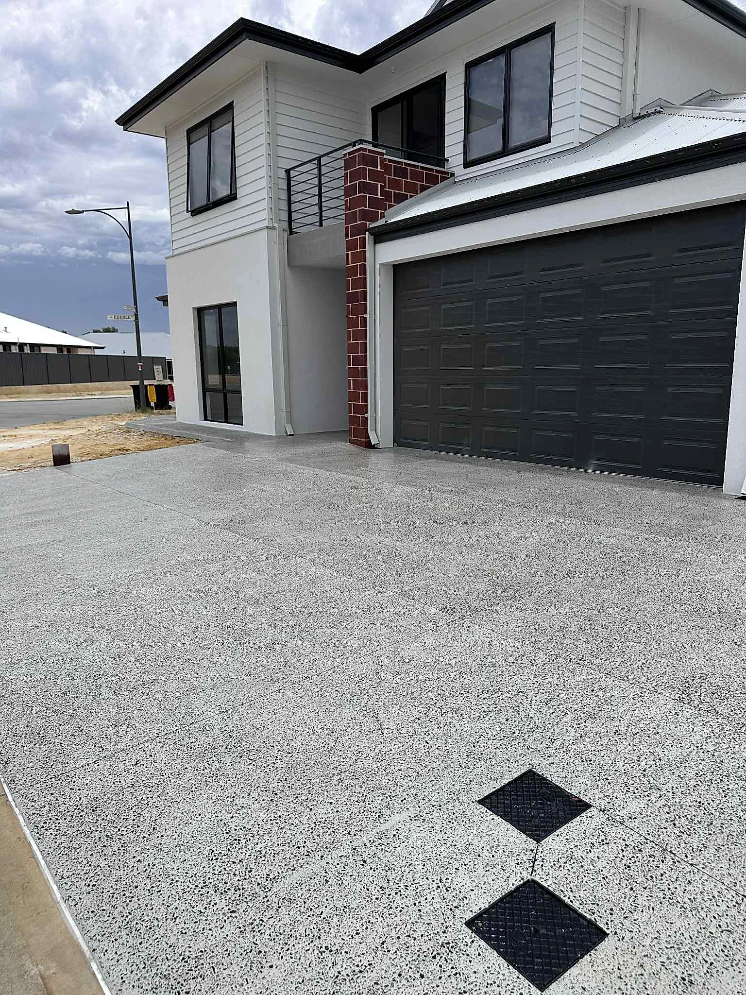 Double driveway in a basalt and pepper mix with dark inlay squares set into the pour, matched to the brick and