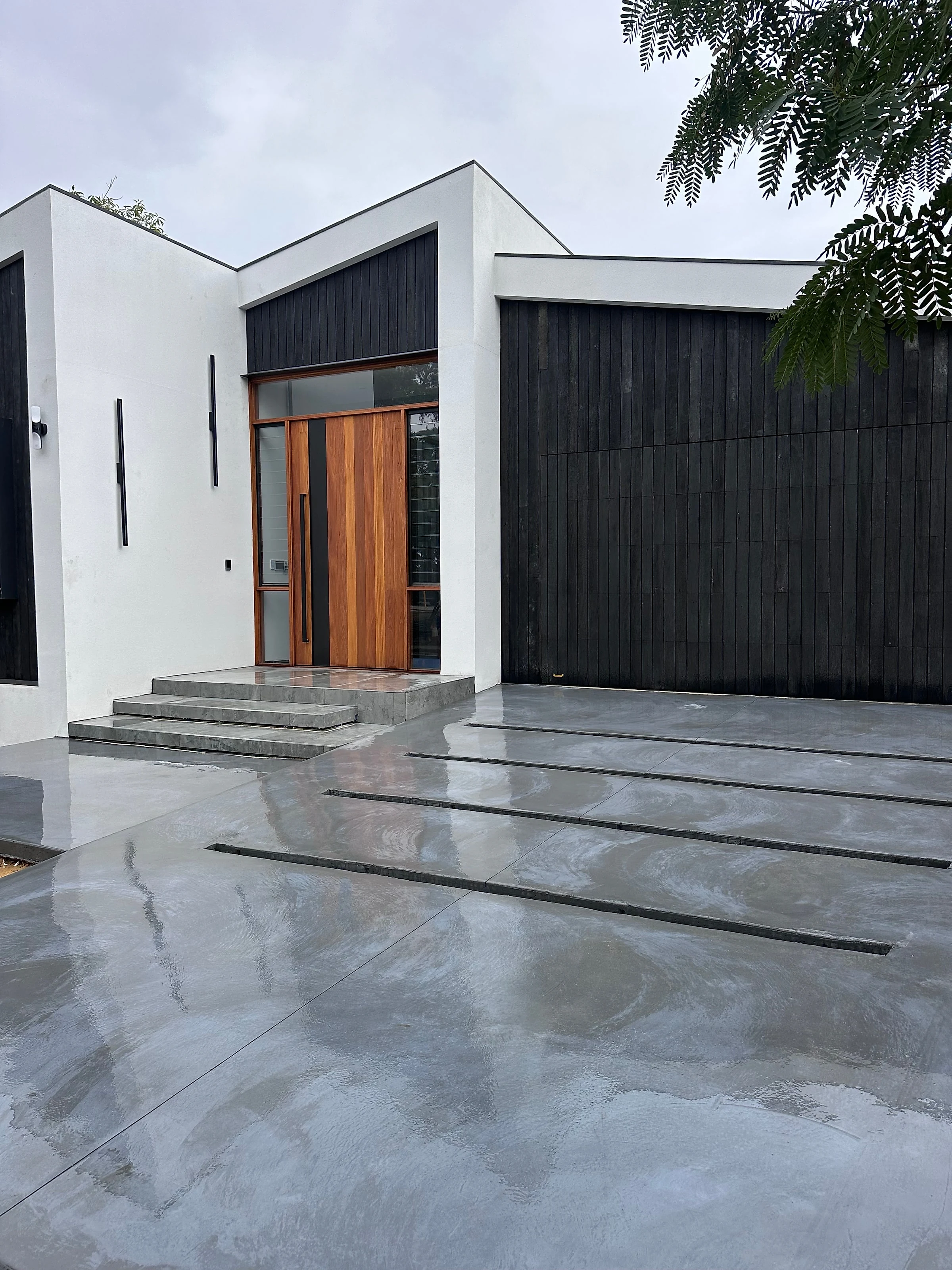 A burnished architectural grey driveway and entry landings, with dark inset joints set out as a deliberate lin