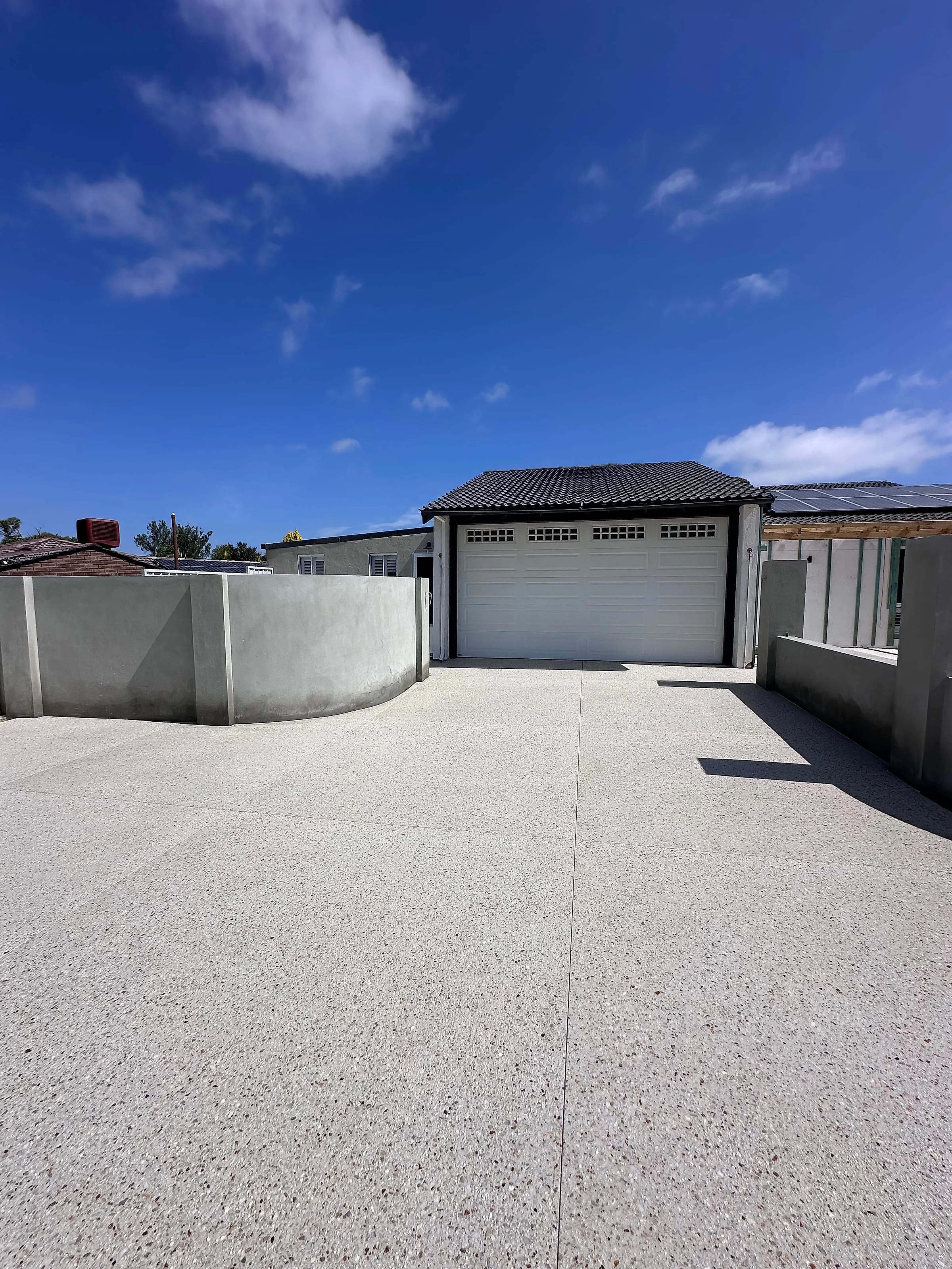 A 200m2 driveway rip out and replace in exposed aggregate, run between curved rendered retaining walls up to a
