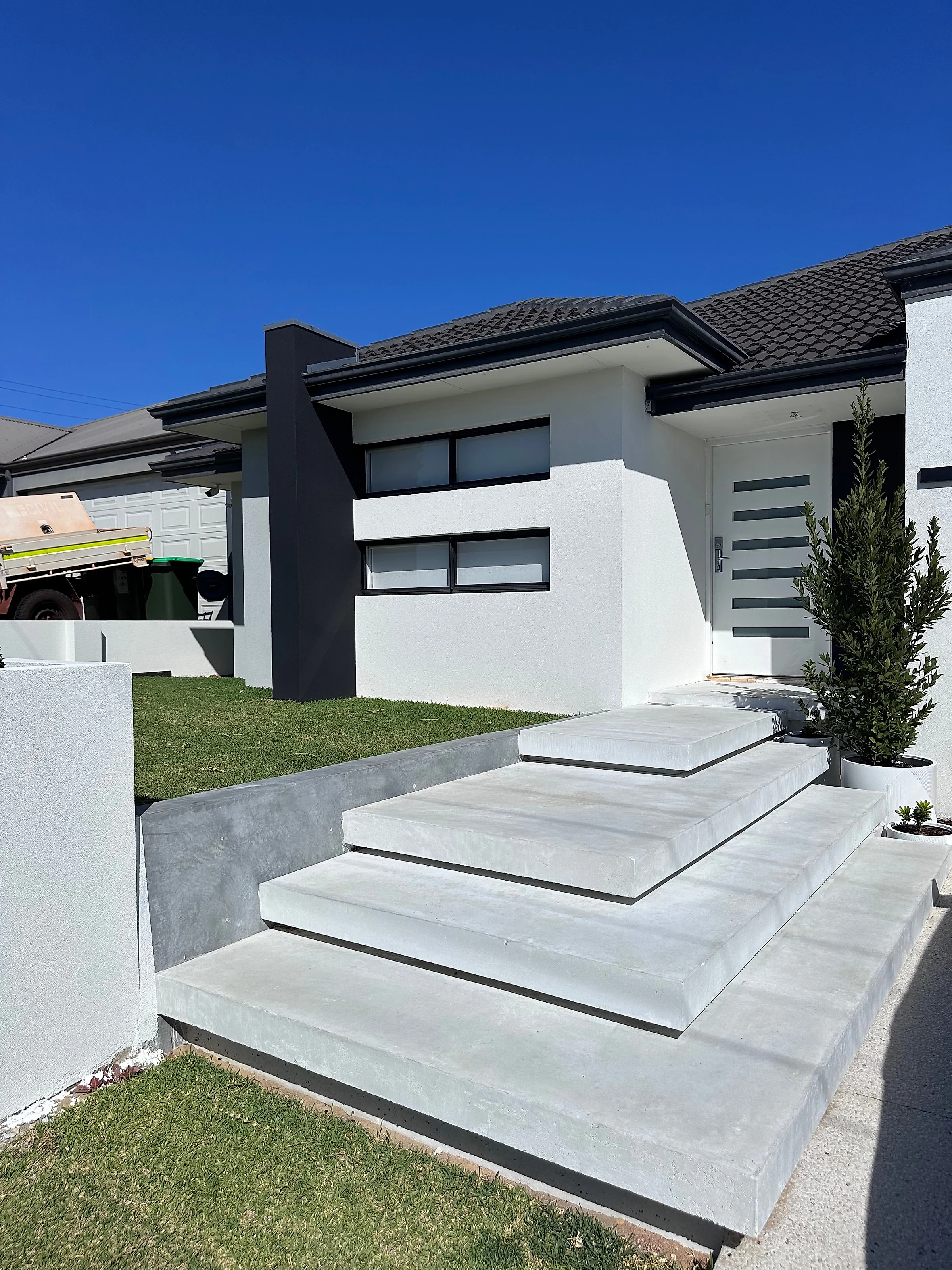Floating entry steps in Holcim Geostone architectural white, rising off a rendered retaining wall to the front