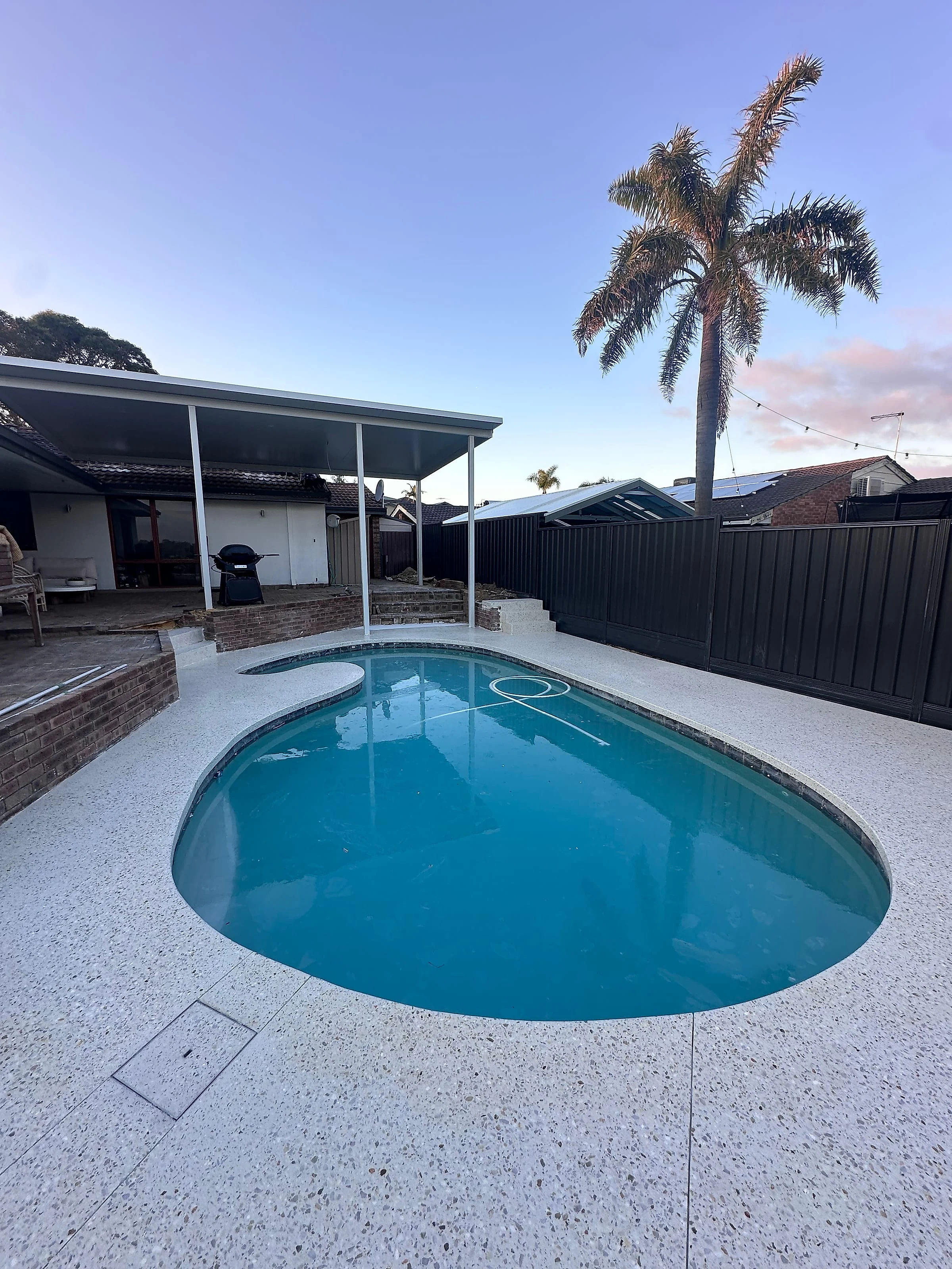 Honed concrete pool surrounds and honed steps wrapping a backyard pool, carried out to the patio so the whole 