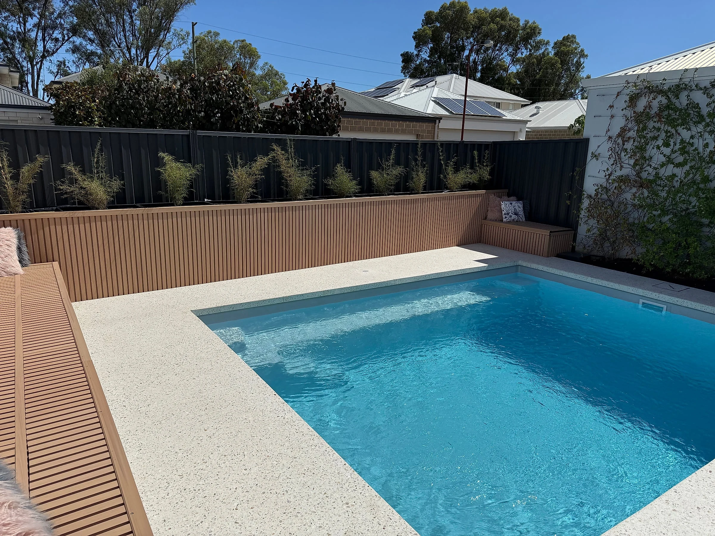 Honed concrete pool surrounds wrapping a backyard pool, run out to the adjoining outdoor living area so the wh