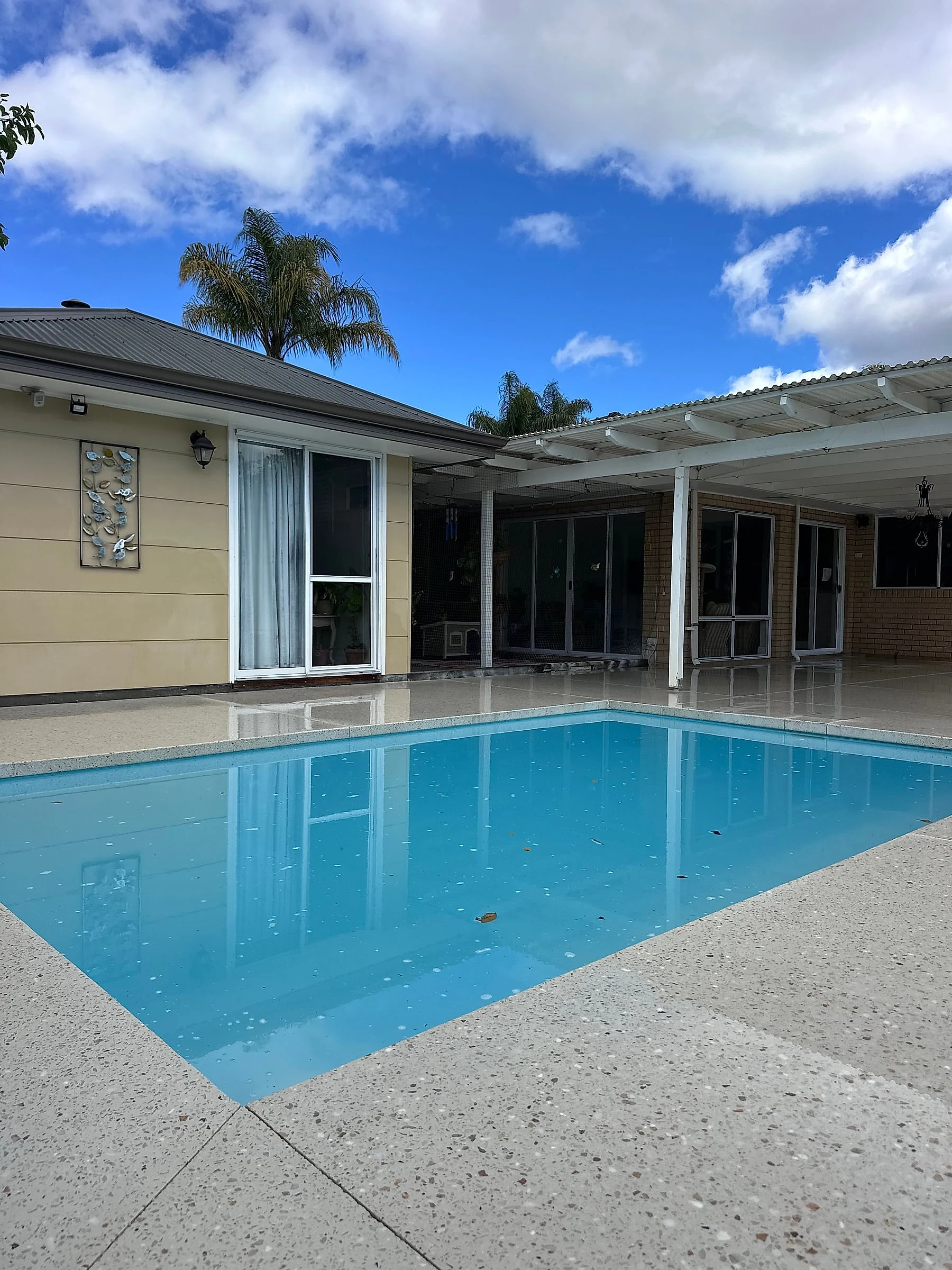 A honed pool surround wrapping a rectangular pool and carried out under the pergola to the back of the house, 