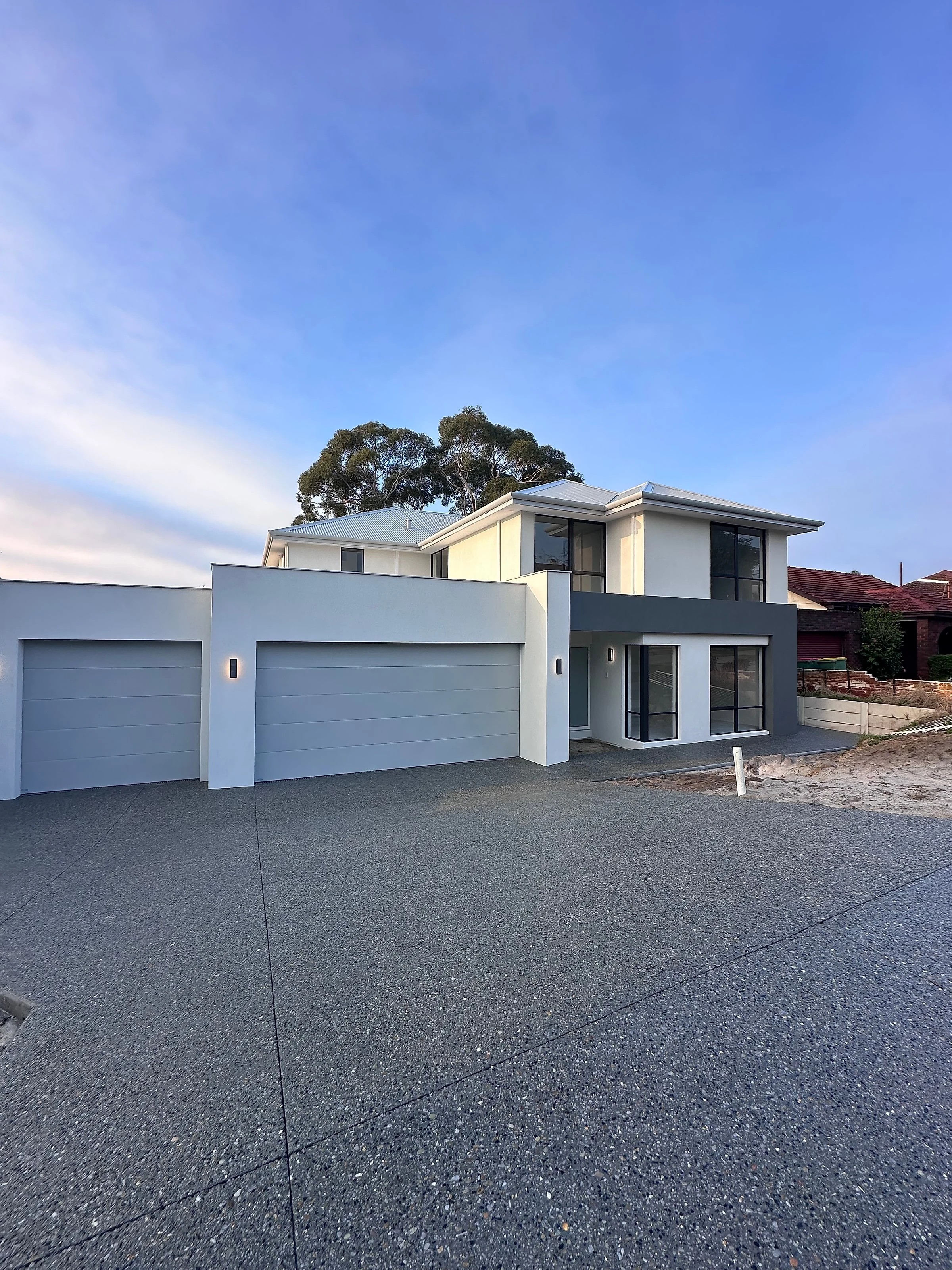 A 150m2 driveway and shared forecourt in Limecrete Kuru Grey serving two townhouses on one sloping block, with