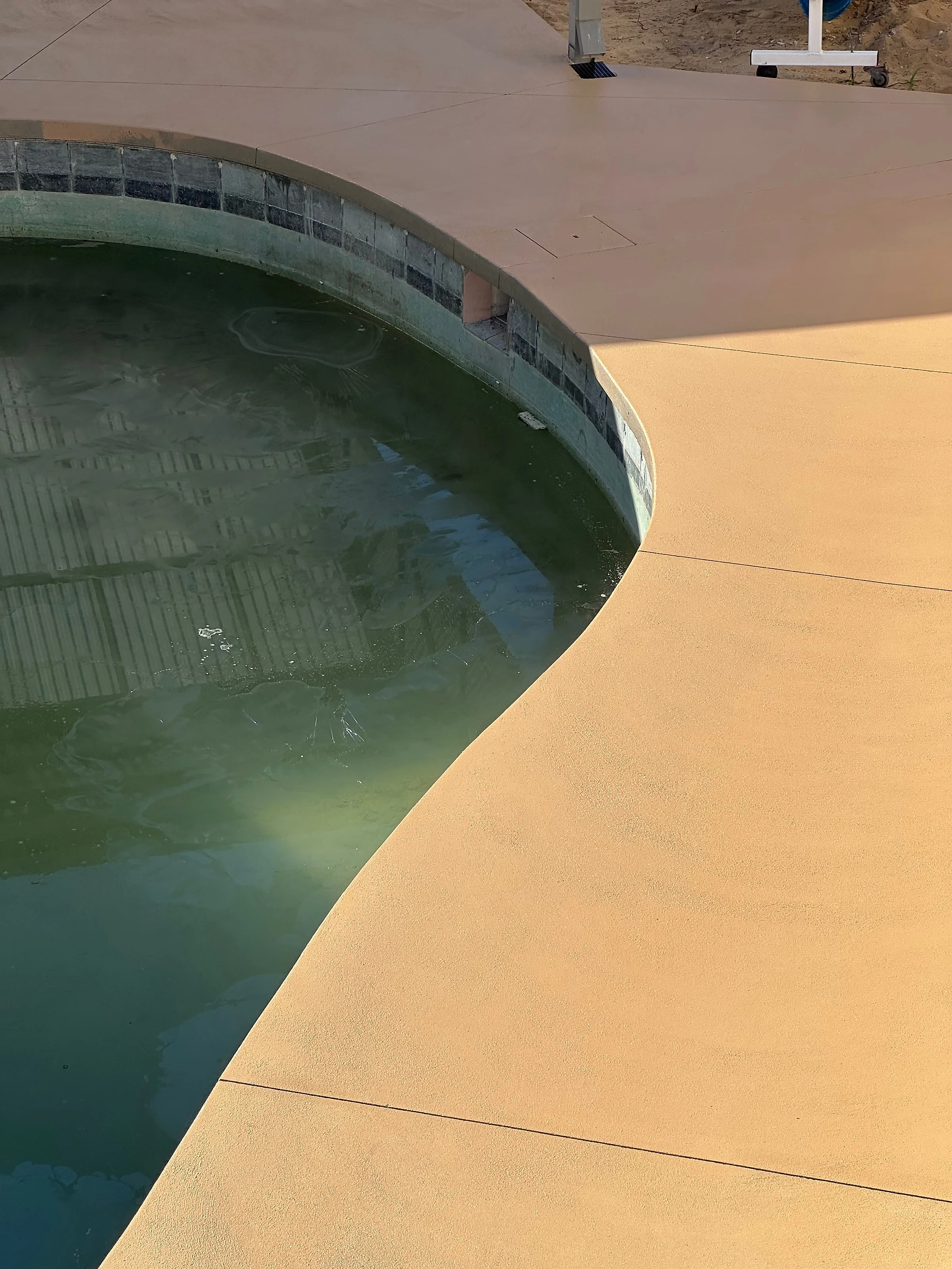 A coloured concrete surround wrapping a kidney shaped pool and running back under the patio, poured to a seaml